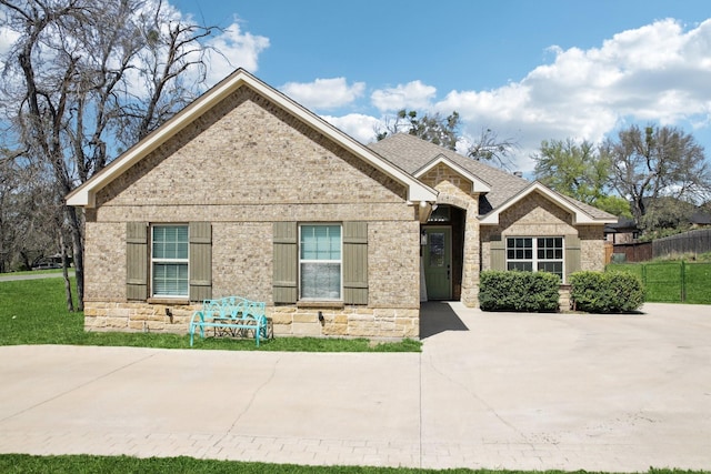 view of front of house featuring roof with shingles, stone siding, a front lawn, brick siding, and fence