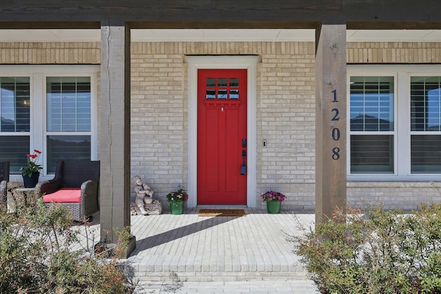 view of exterior entry with brick siding and a porch