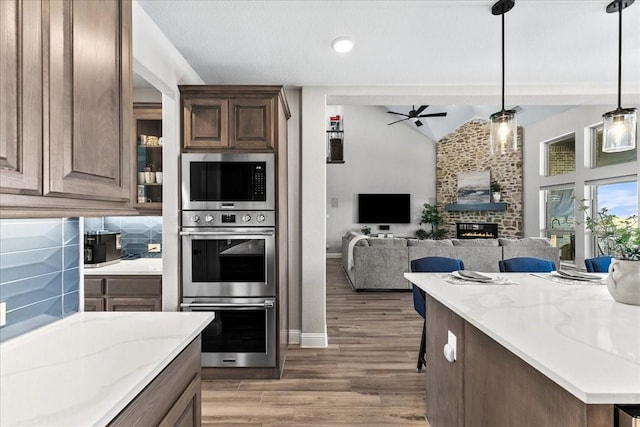 1261 Duke Dr, Prosper, TX 75078 - kitchen with appliances with stainless steel finishes, a warm lit fireplace, wood finished floors, a ceiling fan, and lofted ceiling