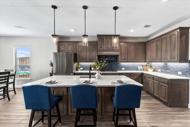 1261 Duke Dr, Prosper, TX 75078 - kitchen featuring freestanding refrigerator, light wood-style flooring, tasteful backsplash, a center island with sink, and recessed lighting