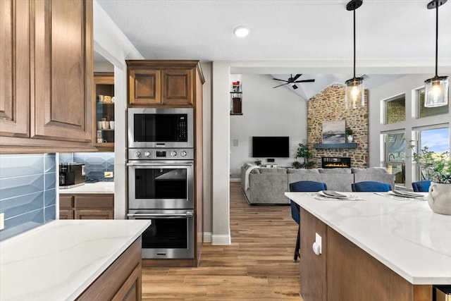 1261 Duke Dr, Prosper, TX 75078 - kitchen featuring light wood-style flooring, ceiling fan, a glass covered fireplace, and stainless steel appliances