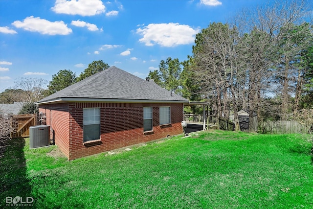 view of home's exterior featuring fence, roof with shingles, brick siding, central AC, and a lawn
