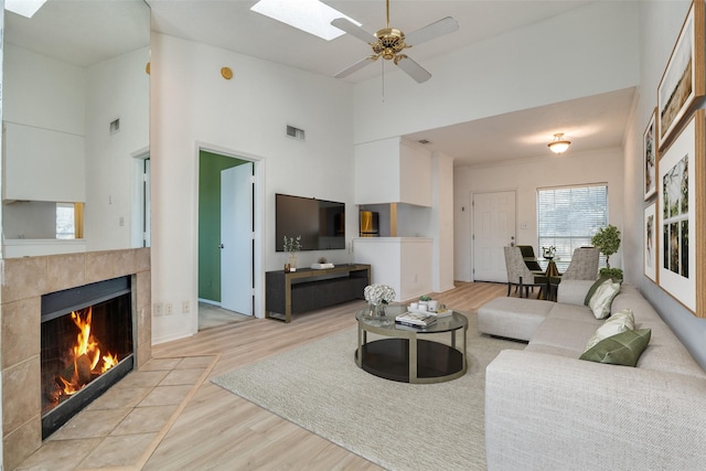 living area featuring high vaulted ceiling, a tiled fireplace, wood finished floors, visible vents, and ceiling fan