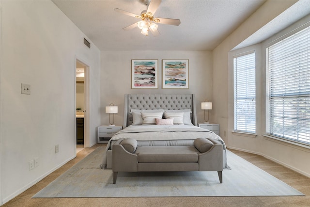 bedroom with visible vents, baseboards, a ceiling fan, light carpet, and ensuite bath