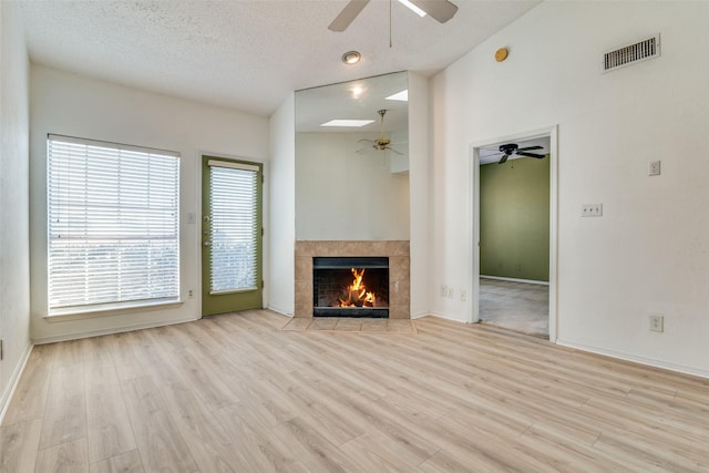unfurnished living room featuring a textured ceiling, visible vents, wood finished floors, a tiled fireplace, and a ceiling fan