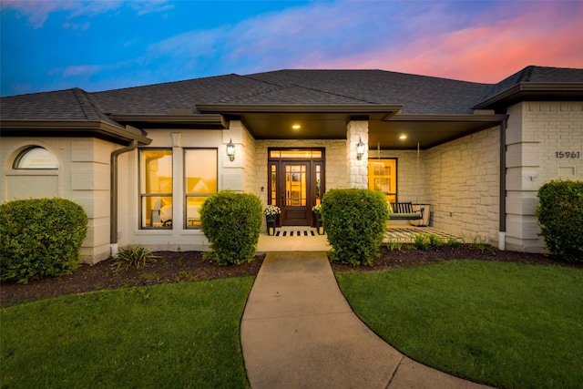 15961 Custer Trl, Frisco, TX 75035 - exterior entry at dusk with a porch, a yard, roof with shingles, and stone siding