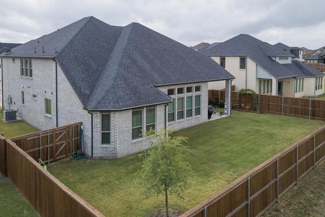 back of house featuring roof with shingles, a lawn, central AC, and brick siding