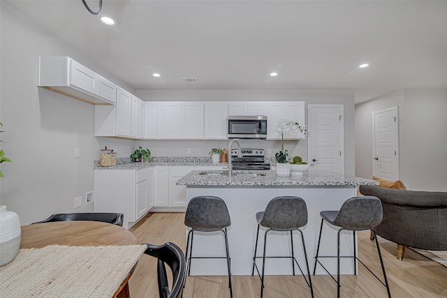 kitchen featuring a sink, white cabinets, stainless steel appliances, and an island with sink