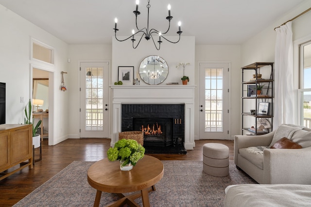 living room featuring baseboards, dark wood-style floors, an inviting chandelier, and a lit fireplace