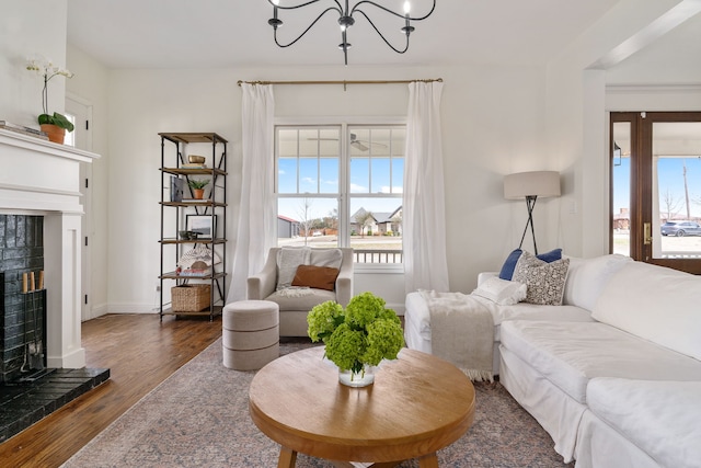 living room featuring a chandelier, wood finished floors, a brick fireplace, and baseboards