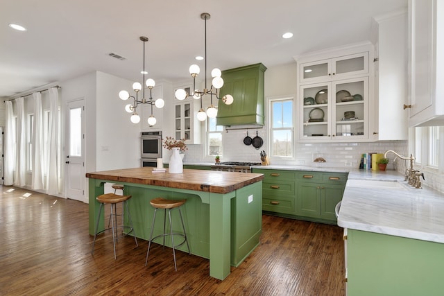 kitchen with custom exhaust hood, green cabinets, butcher block countertops, and a sink