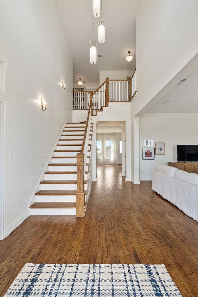 staircase featuring visible vents, baseboards, wood finished floors, and a high ceiling