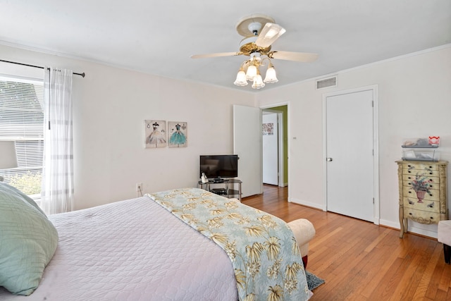 bedroom with crown molding, light wood-type flooring, baseboards, ceiling fan, and visible vents