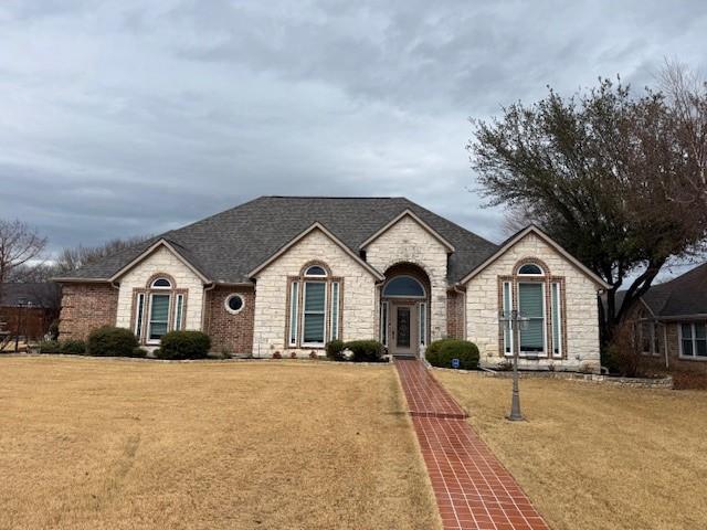 french provincial home featuring stone siding, a shingled roof, and a front lawn