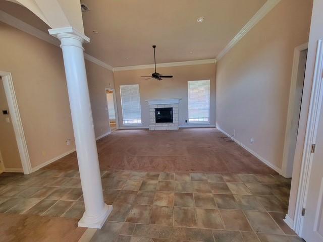 unfurnished living room with crown molding, baseboards, a fireplace, ceiling fan, and decorative columns