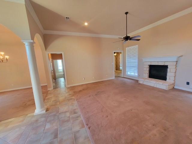 unfurnished living room featuring crown molding, decorative columns, ceiling fan with notable chandelier, arched walkways, and a fireplace