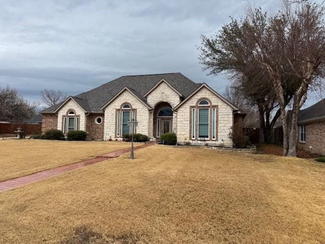 french country home featuring a front lawn and stone siding