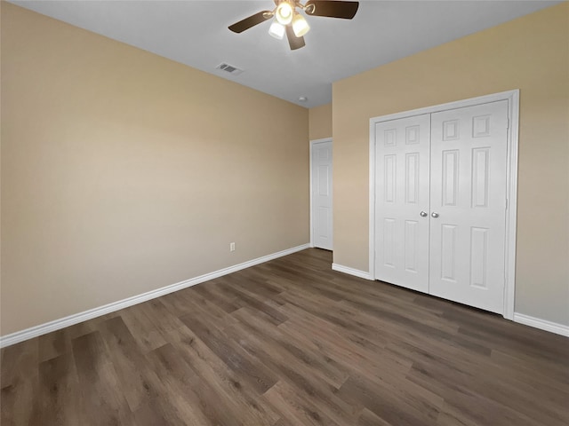 unfurnished bedroom with dark wood-style flooring, a closet, baseboards, and visible vents
