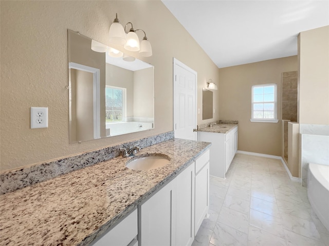 full bath with a bathing tub, baseboards, marble finish floor, two vanities, and a sink