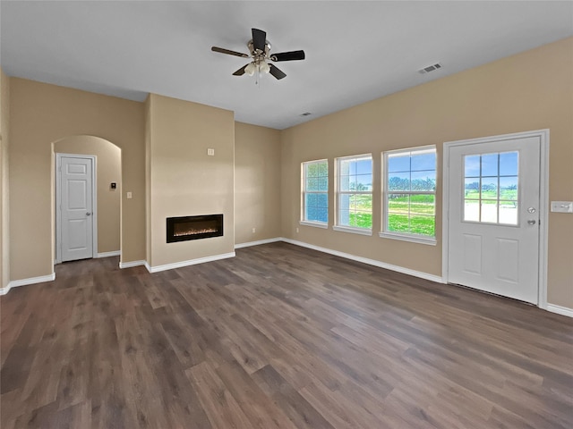 unfurnished living room with baseboards, dark wood finished floors, arched walkways, visible vents, and ceiling fan