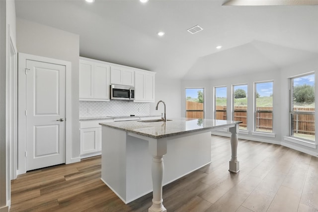 116 Mesa Dr, Glen Rose, TX 76043 - kitchen featuring stainless steel microwave, a sink, light stone counters, an island with sink, and backsplash