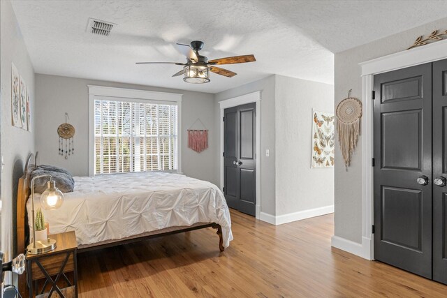bedroom featuring baseboards, visible vents, light wood-style floors, and a textured ceiling