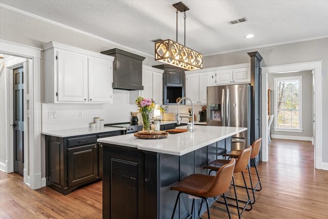 kitchen featuring light countertops, visible vents, white cabinets, stainless steel fridge, and crown molding
