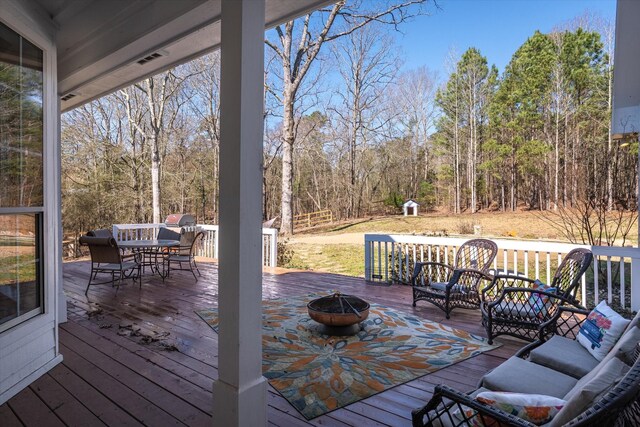 wooden terrace with an outdoor living space with a fire pit, a view of trees, and outdoor dining space