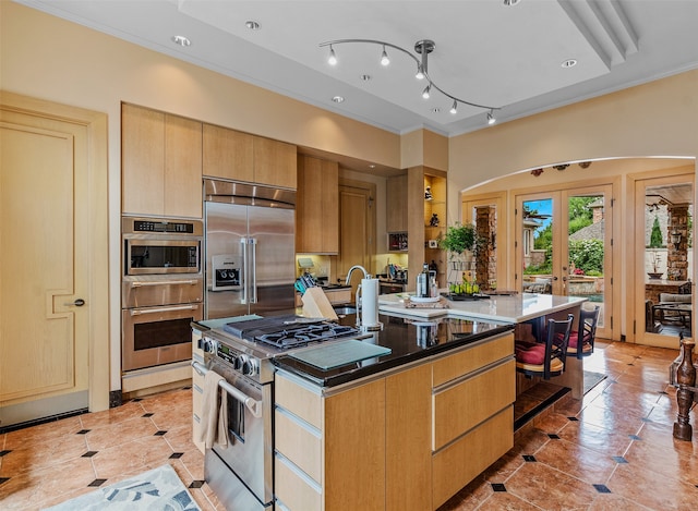 kitchen with ornamental molding, stainless steel appliances, light tile patterned flooring, arched walkways, and a kitchen island with sink