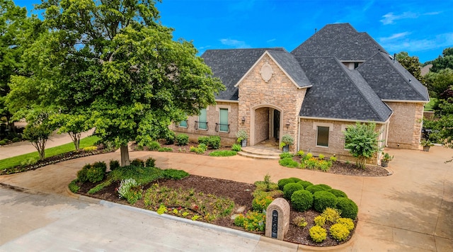 french provincial home with stone siding, curved driveway, and roof with shingles