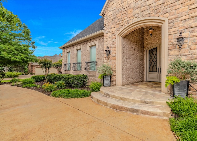 doorway to property featuring brick siding, a porch, and roof with shingles
