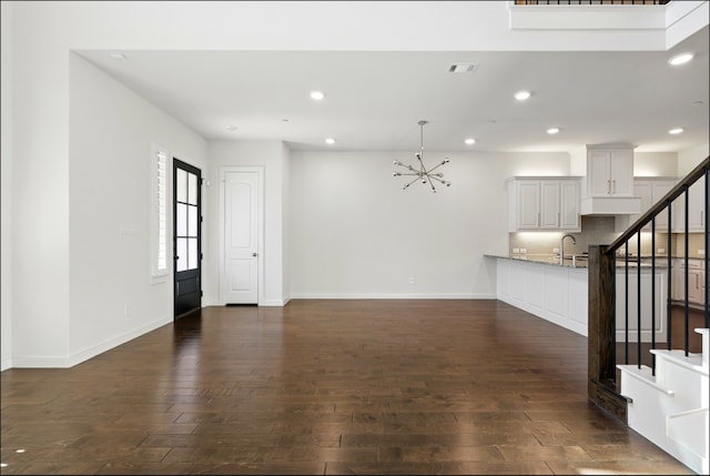 unfurnished living room featuring stairs, a chandelier, dark wood-style floors, and visible vents