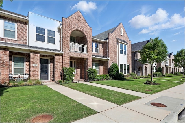townhome / multi-family property featuring brick siding, a balcony, and a front yard