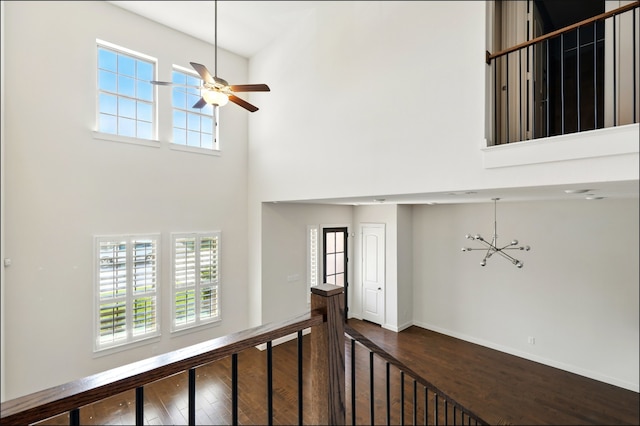 interior space with baseboards, a ceiling fan, a towering ceiling, and wood finished floors