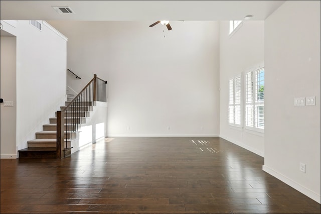 unfurnished living room with a ceiling fan, a towering ceiling, visible vents, dark wood finished floors, and stairs