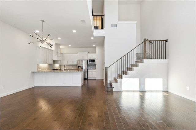 unfurnished living room featuring stairs, a towering ceiling, a chandelier, and dark wood-style floors