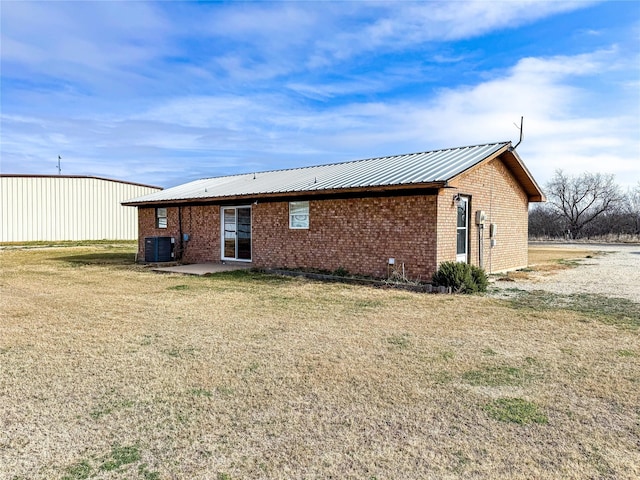 311 S Fir Ave, Munday, TX 76371 - rear view of house featuring metal roof, a patio, central AC, brick siding, and a yard