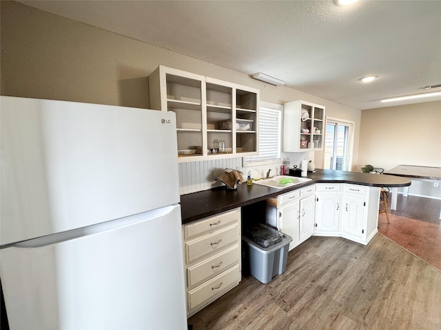 311 S Fir Ave, Munday, TX 76371 - kitchen with a sink, freestanding refrigerator, wood finished floors, a peninsula, and dark countertops