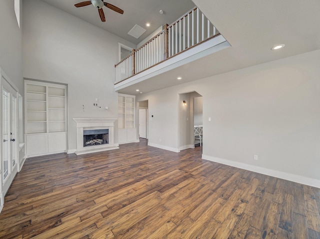 unfurnished living room with baseboards, a towering ceiling, wood finished floors, recessed lighting, and a ceiling fan