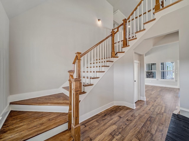 stairs with baseboards, a high ceiling, and wood finished floors