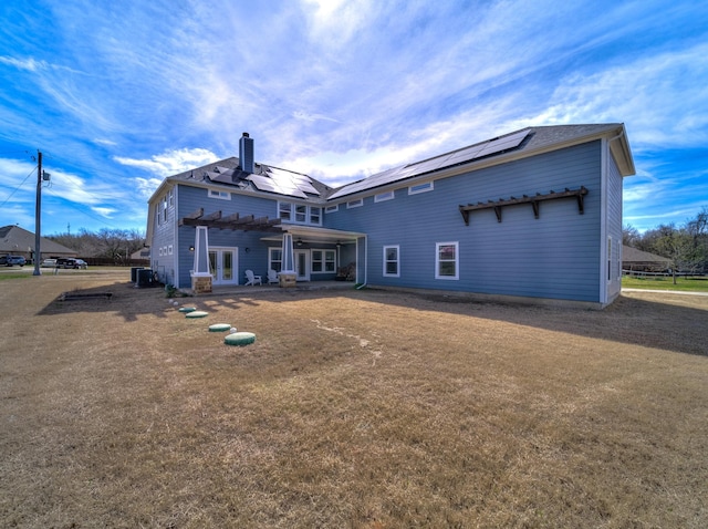 back of property featuring central AC unit, roof mounted solar panels, a chimney, french doors, and a patio area
