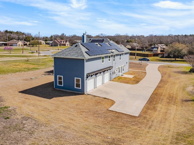 view of side of property featuring roof with shingles, a residential view, driveway, a garage, and roof mounted solar panels