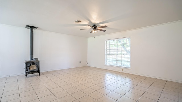 unfurnished living room featuring light tile patterned floors, a ceiling fan, visible vents, a wood stove, and crown molding