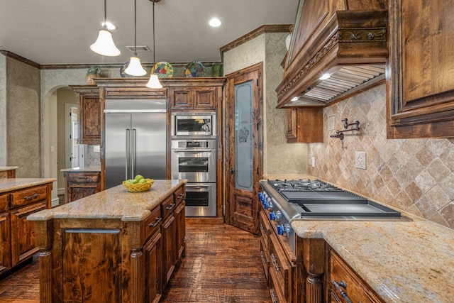 kitchen featuring built in appliances, custom exhaust hood, dark wood-style floors, arched walkways, and ornamental molding