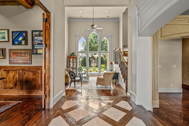 foyer entrance featuring inlaid floor details, crown molding, baseboards, a ceiling fan, and a towering ceiling