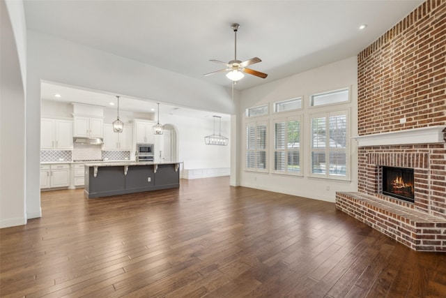 3612 Green Mountain Pl, Mckinney, TX 75070 - unfurnished living room with a brick fireplace, a ceiling fan, dark wood-style floors, and a chandelier