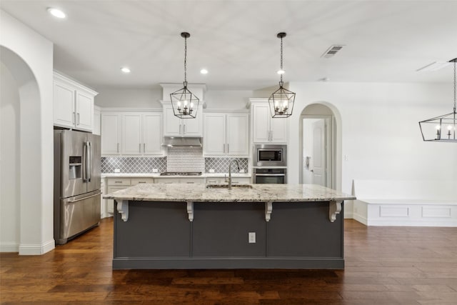 3612 Green Mountain Pl, Mckinney, TX 75070 - kitchen featuring appliances with stainless steel finishes, under cabinet range hood, a sink, arched walkways, and tasteful backsplash