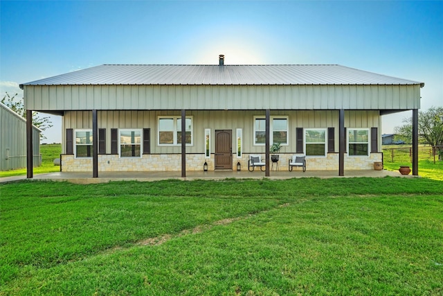 rear view of house featuring stone siding, board and batten siding, a yard, and metal roof