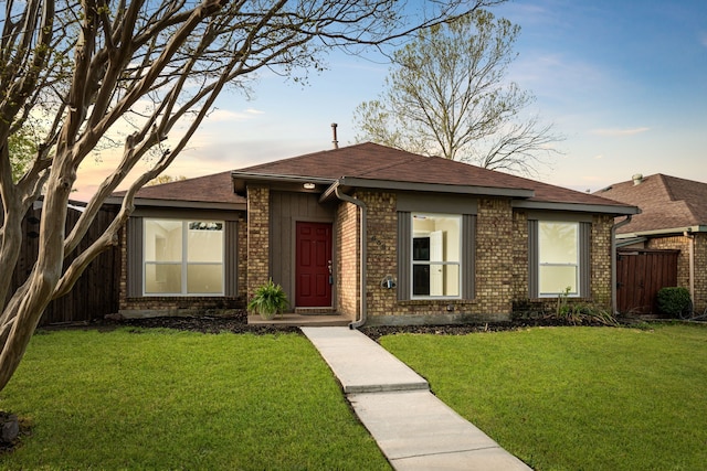 view of front of property with brick siding, a front lawn, fence, and a shingled roof