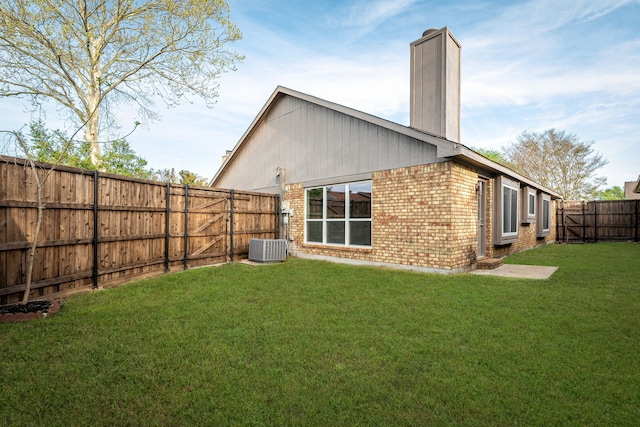rear view of property with brick siding, a lawn, central AC, and a fenced backyard